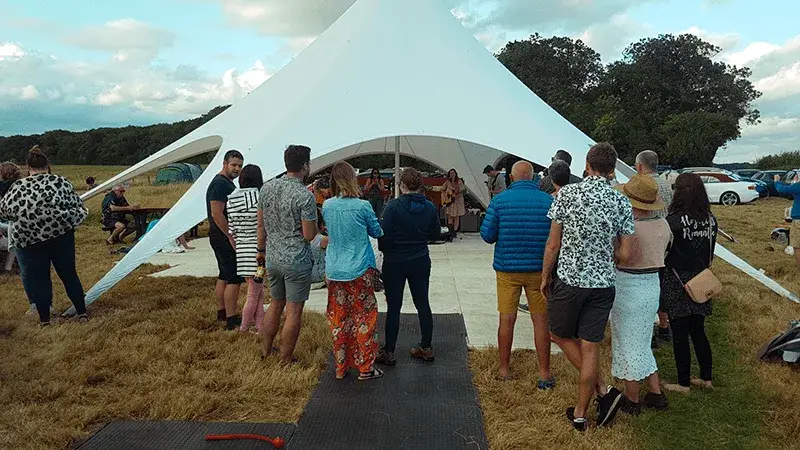 A crowd watches a band perform under a large white StarShade events tent in a grassy field at an outdoor festival.