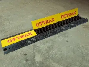 Black cable protector ramp with yellow covers featuring "GTTRAX" text, lying on a grey concrete floor.