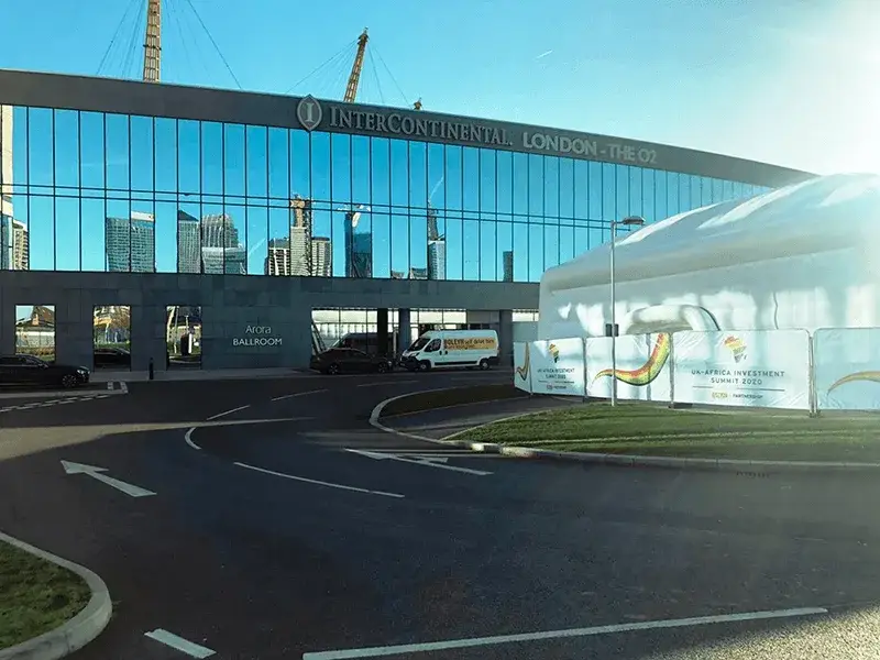 Intercontinental London - The O2 hotel with reflective glass showing city skyline. A white tent with Heras fencing with banners on in front.