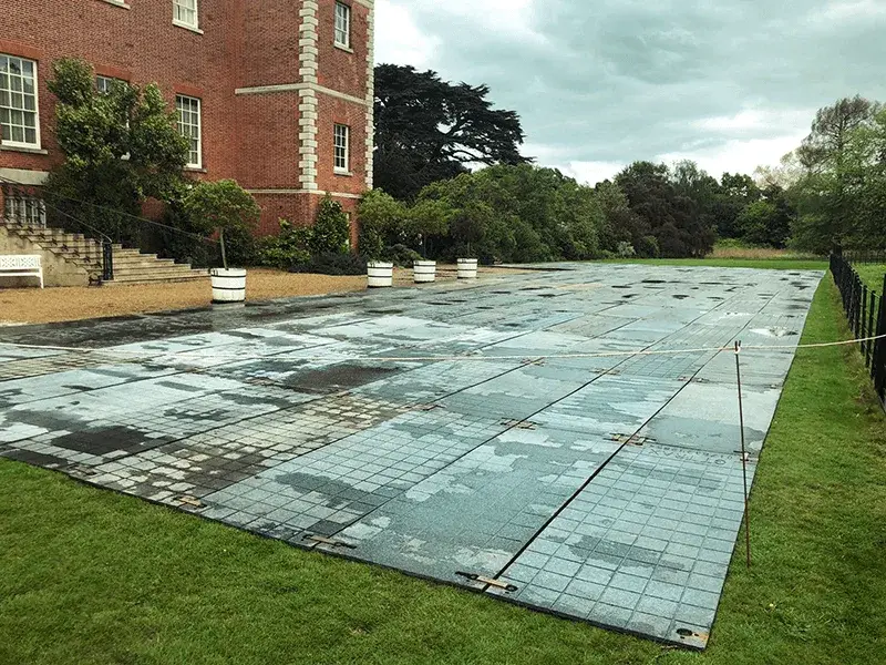 Large wet modular PowerTrax 20 panels cover a green lawn next to a red brick building under an overcast sky.