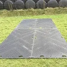Black EuroMats ground mats laid on grass with rows of black hay bales in the distance.