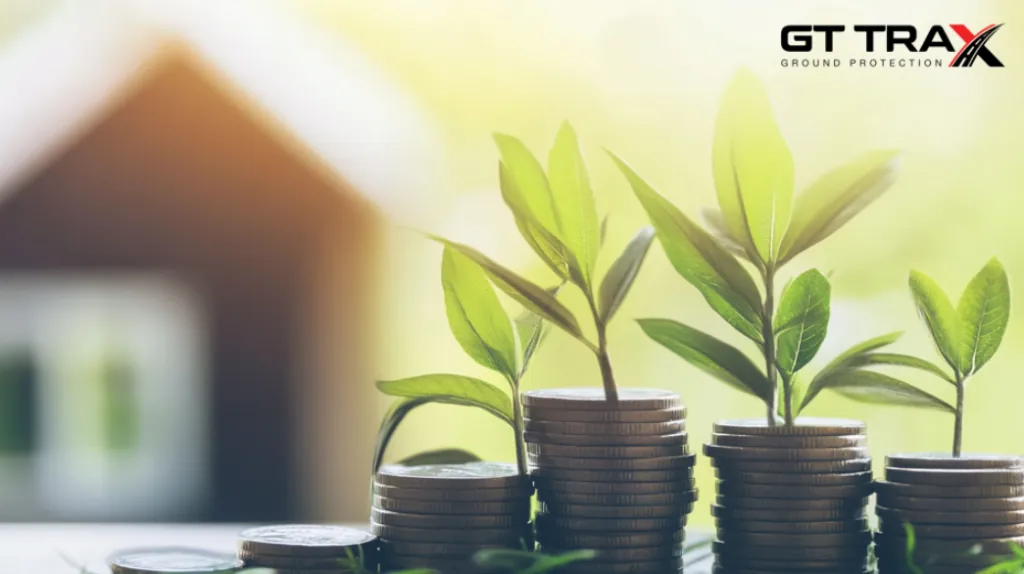 Small green plants sprout from gradually taller coin stacks. A blurred house is in the sunlit background. GT Trax logo in the corner