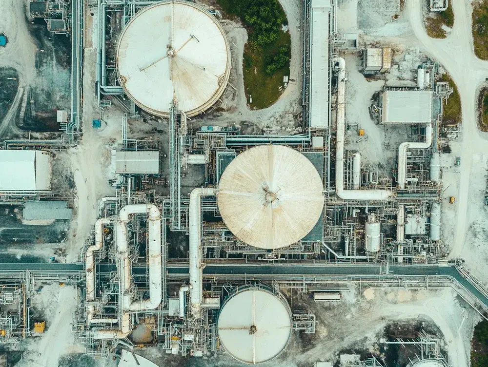 Aerial view of a vast industrial plant featuring large circular storage tanks, complex networks of pipes, and various buildings.