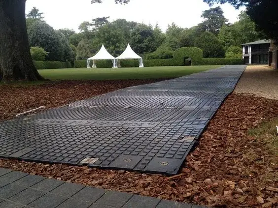 PowerTrax 40 temporary black mat path over wood chips, leading to a green lawn with two white event tents and trees.
