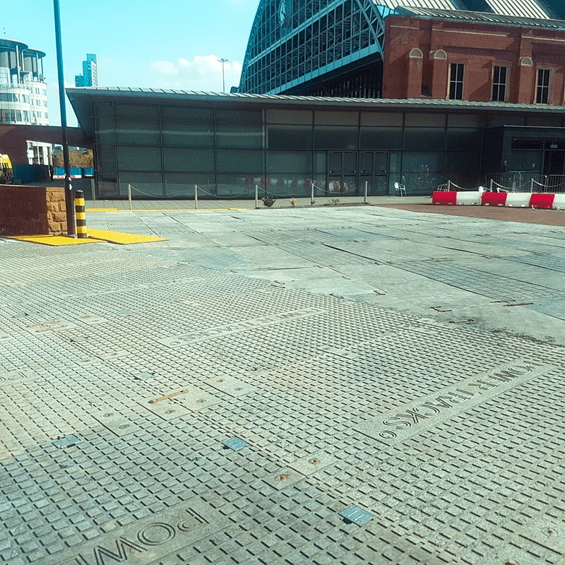 Textured grey PowerTrax 40 paving in an urban square. A modern glass building sits in front of an old red brick building with a large metal roof.