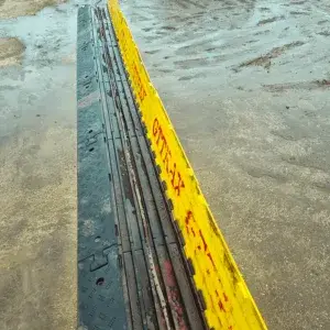 Cable protector laid forward with yellow top open with 'GT TRAX' markings, laid on wet, muddy ground.