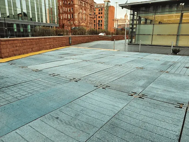 Modular blue-gray PowerTrax 20 ground mats with grid and striped textures. Urban setting with glass and brick buildings, and a low brick wall.