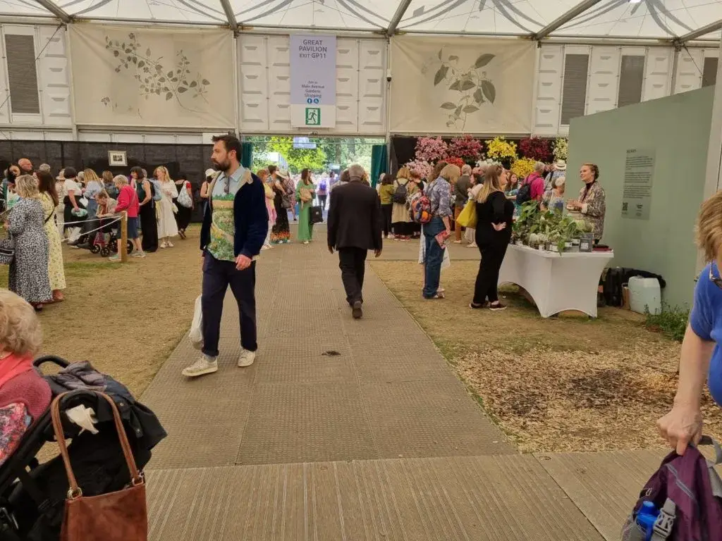Crowd of people in a large exhibition tent with LiteTrax flooring walkway and plant and flower displays. A man in a blue jacket stands in the foreground.
