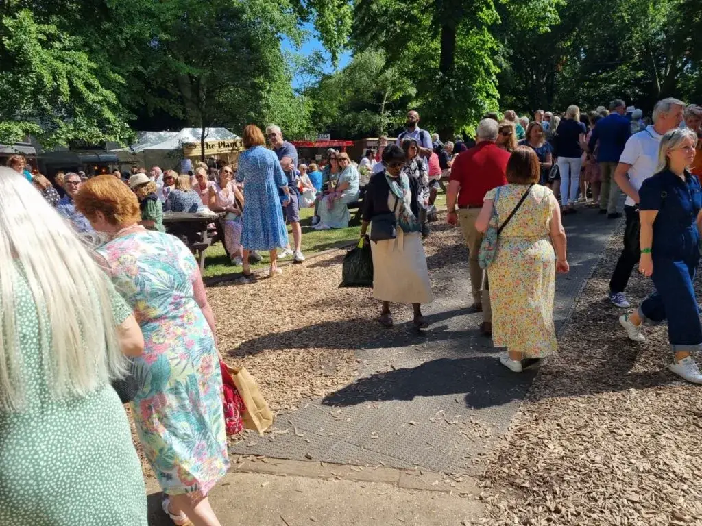 Large crowd of adults walking and mingling at an outdoor summer event with trees, tents, and LuxTrax paths.
