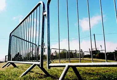Close-up of a silver crowd control barrier on green grass under a blue sky.