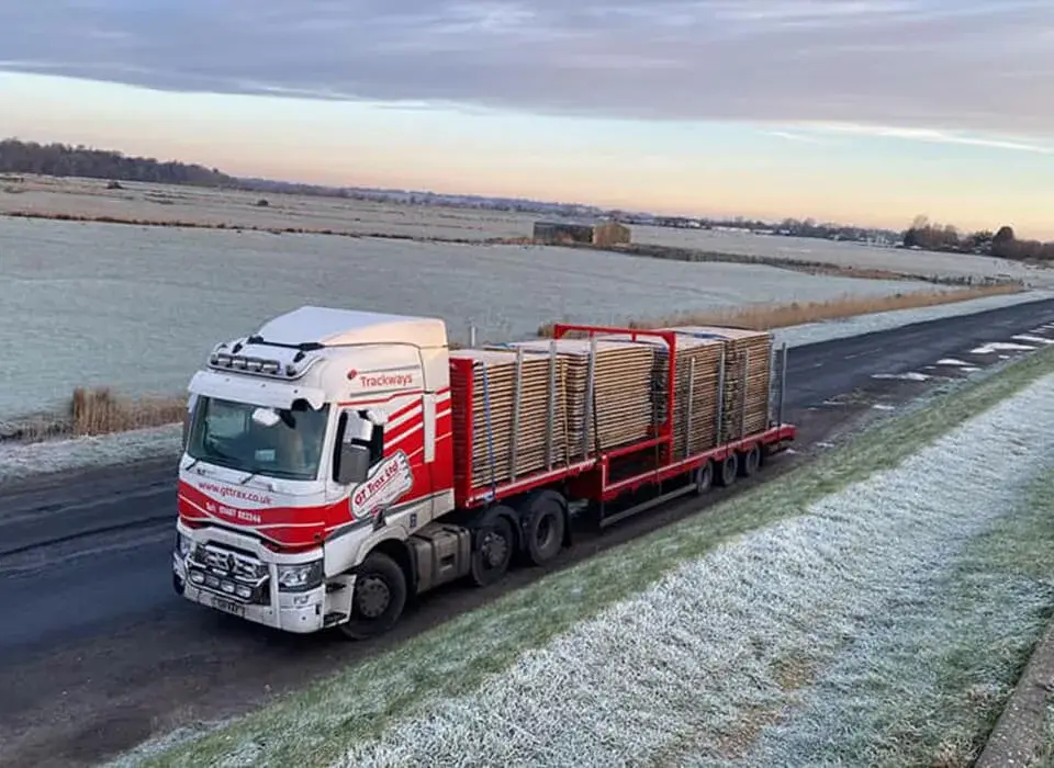 White and red GT Trax  truck hauling stacked PowerTrax 60 panels on a rural road with frost-covered fields.