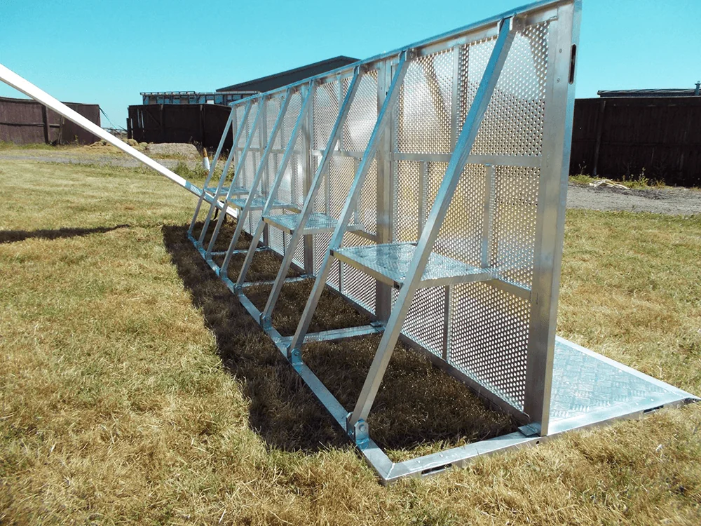 Long silver metal Stage & Pit barrier with perforated panels on dry grass under a clear blue sky.