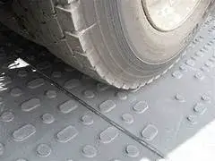 Close-up of a large tire resting on a grey textured TuffTrak mat with raised oval and circular patterns.