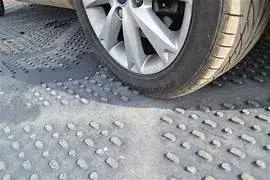 Close-up of a silver car wheel and tire resting on a grey, textured EuroMats mat with many small, oval-shaped bumps.
